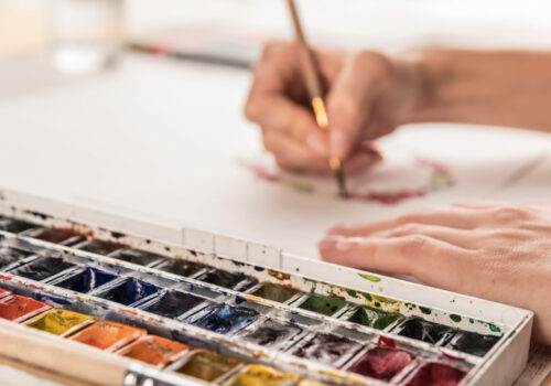 Young artist drawing flowers pattern with watercolor paint and brush at workplace