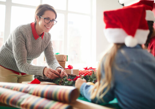 Talking to daughters Happy young woman finishing up with coniferous wreath while looking at her little daughters