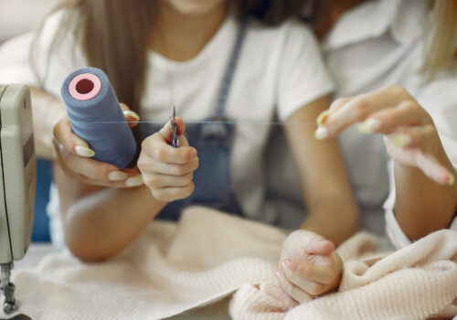 Mother with little daughter sew clothes in the factory Mother with daughter at the factory. Family with a fabric.